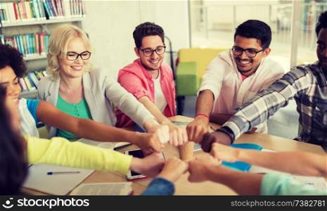 education, school, teamwork and people concept - group of international students sitting at table and making fist bump. group of international students making fist bump