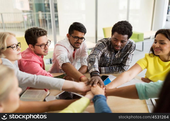 education, school, teamwork and people concept - group of international students with hands on top of each other sitting at table