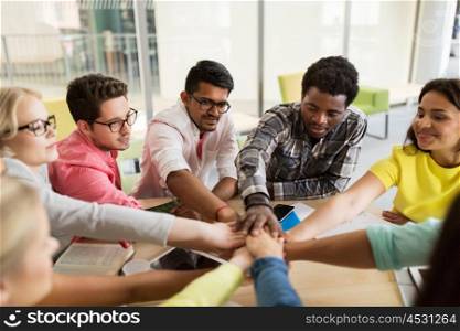 education, school, teamwork and people concept - group of international students with hands on top of each other sitting at table