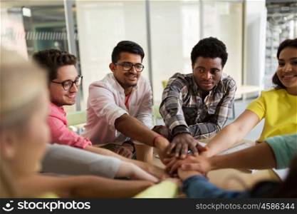 education, school, teamwork and people concept - group of international students with hands on top of each other sitting at table