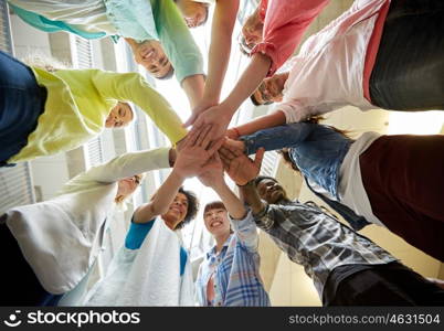 education, school, teamwork and people concept - group of international students with hands on top of each other over table