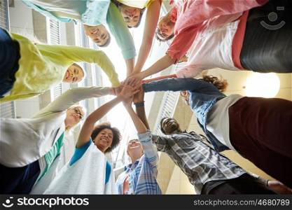 education, school, teamwork and people concept - group of international students with hands on top of each other over table