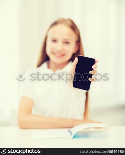 education, school, technology and internet concept - little student girl with notebook and black blank smartphone screen at school
