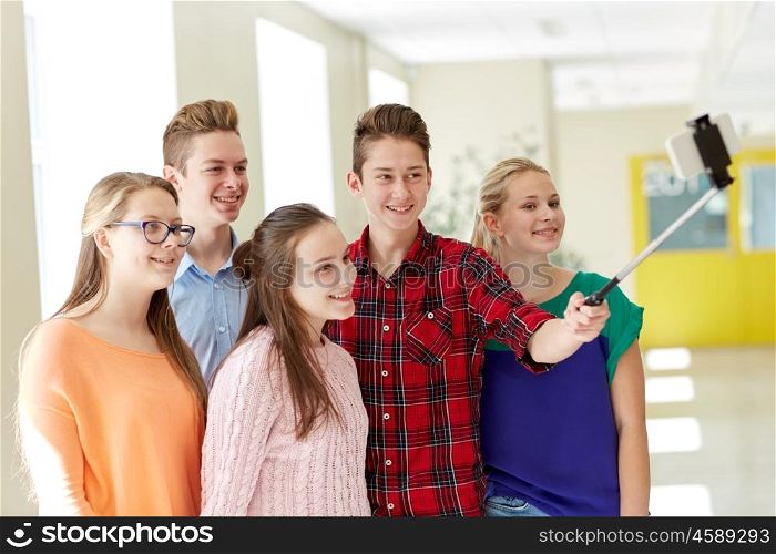 education, school, technology and people concept - group of happy smiling students taking picture with smartphone selfie stick in corridor