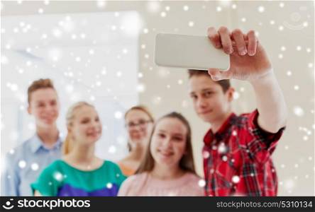 education, school, technology and people concept - group of happy smiling students taking selfie with smartphone in corridor over snow. group of students taking selfie with smartphone