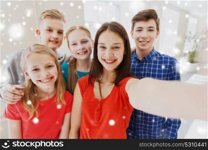 education, school, technology and people concept - group of happy smiling students taking selfie in corridor over snow. group of students taking selfie