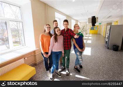 education, school, technology and people concept - group of happy smiling students taking picture with smartphone selfie stick in corridor