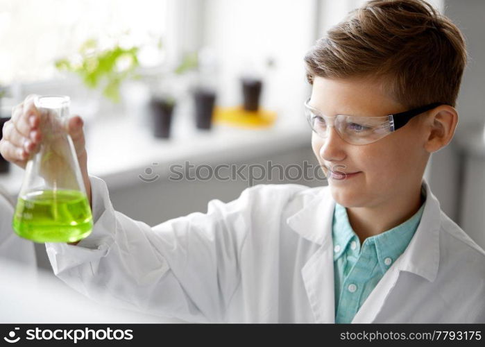 education, science and children concept - boy in goggles with test tube studying chemistry at school laboratory. boy with test tube studying chemistry at school