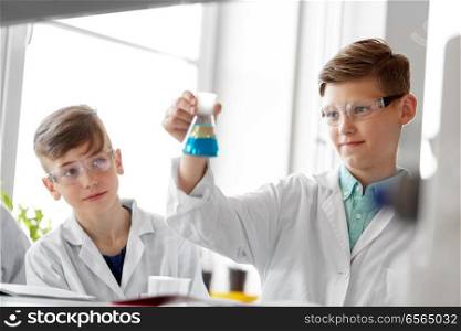 education, science and children concept - boys in goggles with test tube studying chemistry at school laboratory. boys with test tube studying chemistry at school