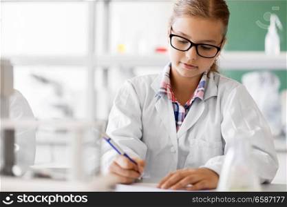 education, science and children concept - close up of girl studying chemistry at school laboratory and writing to workbook. girl studying chemistry at school laboratory