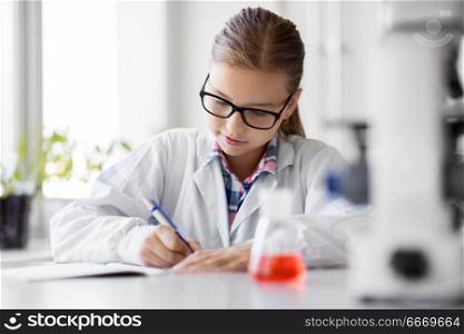 education, science and children concept - close up of girl studying chemistry at school laboratory and writing to workbook. girl studying chemistry at school laboratory. girl studying chemistry at school laboratory