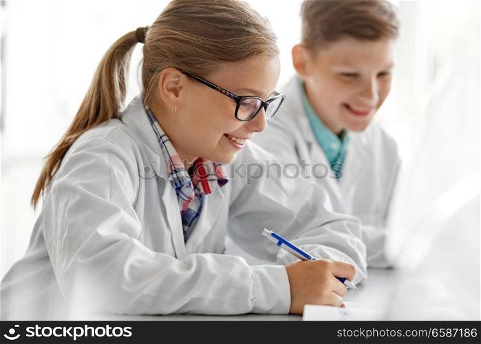 education, science and children concept - close up of happy girl studying chemistry at school laboratory and writing to workbook. happy girl studying chemistry at school laboratory