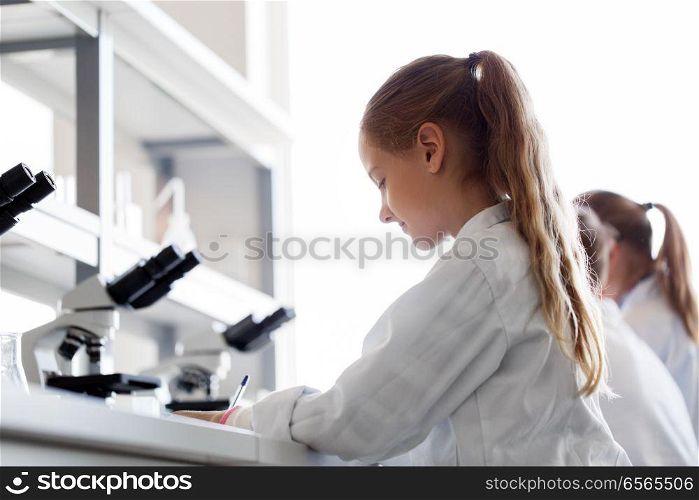 education, science and children concept - girl studying chemistry at school laboratory and writing. girl studying chemistry at school laboratory