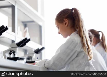 education, science and children concept - girl studying chemistry at school laboratory and writing. girl studying chemistry at school laboratory