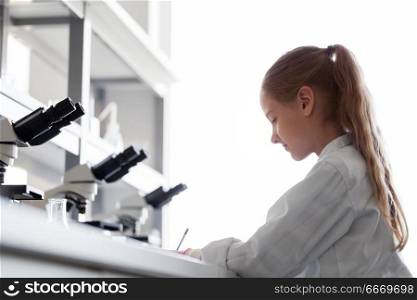 education, science and children concept - girl studying chemistry at school laboratory and writing. girl studying chemistry at school laboratory. girl studying chemistry at school laboratory