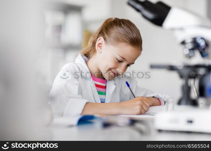 education, science and children concept - girl studying chemistry at school laboratory and writing to workbook. girl studying chemistry at school laboratory