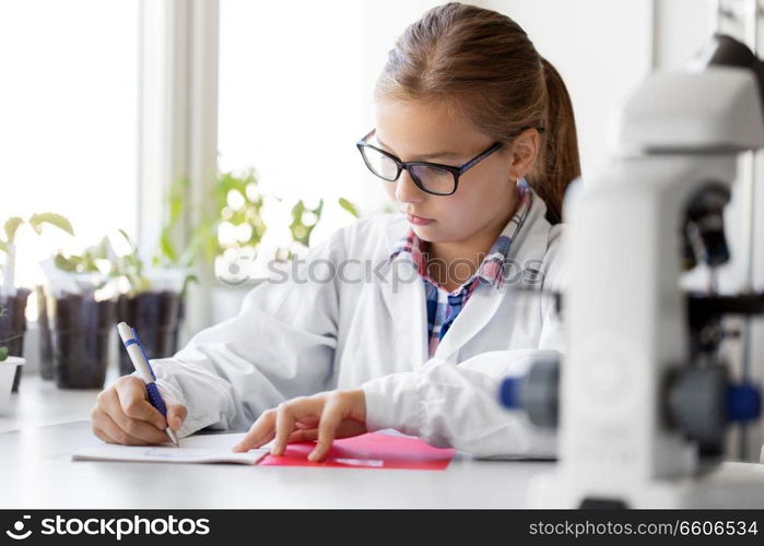 education, science and children concept - girl studying chemistry at school laboratory and writing to workbook. girl studying chemistry at school laboratory