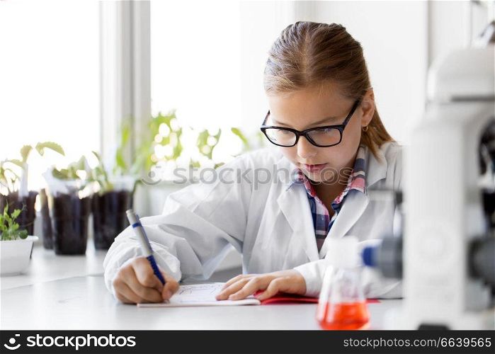 education, science and children concept - girl studying chemistry at school laboratory and writing to workbook. girl studying chemistry at school laboratory