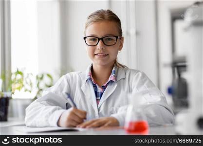 education, science and children concept - girl studying chemistry at school laboratory and writing to workbook. girl studying chemistry at school laboratory. girl studying chemistry at school laboratory