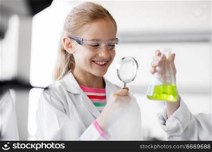 education, science and children concept - girl with magnifier studying test tube with chemical at school laboratory. girl studying test tube at school laboratory. girl studying test tube at school laboratory