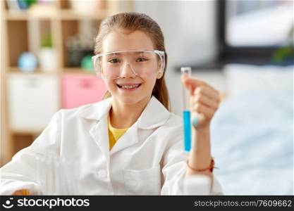 education, science and children concept - happy smiling girl in goggles with test tube studying chemistry at home laboratory. girl with test tube studying chemistry at home