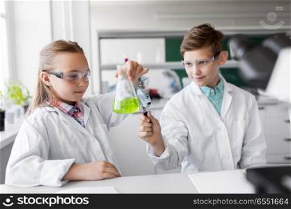 education, science and children concept - kids or students with test tube and magnifier studying chemistry at school laboratory. kids with flask and magnifier at chemistry class. kids with flask and magnifier at chemistry class