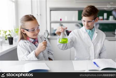 education, science and children concept - kids or students with test tube and magnifier studying chemistry at school laboratory. kids with flask and magnifier at chemistry class. kids with flask and magnifier at chemistry class