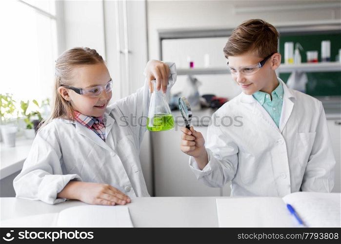 education, science and children concept - kids or students with test tube and magnifier studying chemistry at school laboratory. kids with flask and magnifier at chemistry class