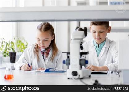education, science and children concept - kids studying chemistry at school laboratory and writing to workbooks. kids studying chemistry at school laboratory. kids studying chemistry at school laboratory