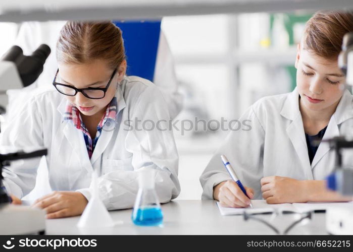 education, science and children concept - kids studying chemistry at school laboratory and writing to workbooks. kids studying chemistry at school laboratory