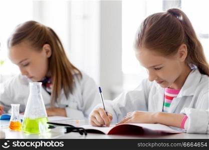 education, science and children concept - kids studying chemistry at school laboratory and writing to workbooks. kids studying chemistry at school laboratory