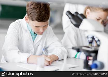 education, science and children concept - kids studying chemistry at school laboratory and writing to workbooks. kids studying chemistry at school laboratory. kids studying chemistry at school laboratory