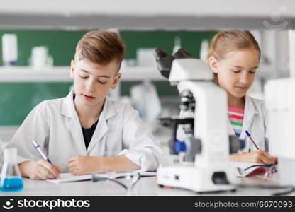 education, science and children concept - kids studying chemistry at school laboratory and writing to workbooks. kids studying chemistry at school laboratory. kids studying chemistry at school laboratory