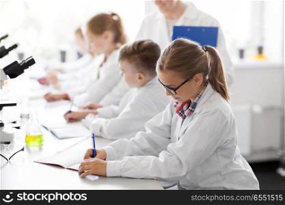 education, science and children concept - teacher and kids or students studying chemistry at school laboratory and writing to workbooks. teacher and students studying chemistry at school. teacher and students studying chemistry at school
