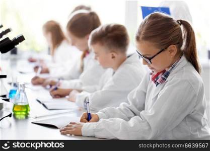 education, science and children concept - teacher and kids studying chemistry at school laboratory and writing to workbooks. kids studying chemistry at school laboratory
