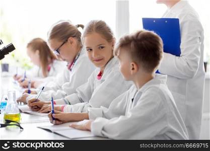 education, science and children concept - teacher and kids studying chemistry at school laboratory and writing to workbooks. kids studying chemistry at school laboratory. kids studying chemistry at school laboratory