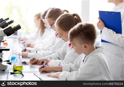 education, science and children concept - teacher and kids studying chemistry at school laboratory and writing to workbooks. kids studying chemistry at school laboratory. kids studying chemistry at school laboratory