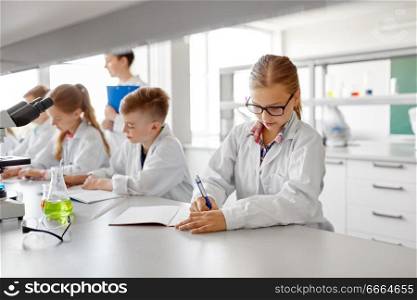 education, science and children concept - teacher and students studying chemistry at school laboratory and writing to workbooks. teacher and students studying chemistry at school