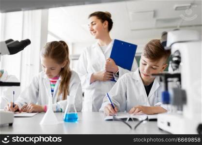 education, science and children concept - teacher and students studying chemistry at school laboratory and writing to workbooks. teacher and students studying chemistry at school. teacher and students studying chemistry at school