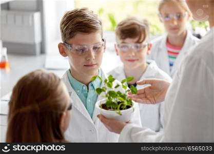 education, science and school concept - students and teacher with plant at biology class. students and teacher with plant at biology class