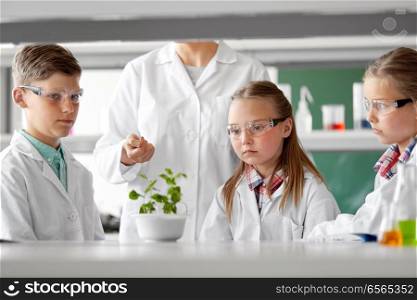 education, science and school concept - students and teacher with plant at biology class. students and teacher with plant at biology class