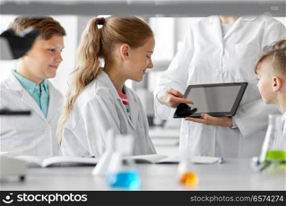 education, science and technology concept - chemistry teacher showing tablet pc computer to kids or students at school laboratory. teacher with tablet pc and kids at chemistry class