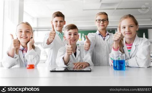 education, science and technology concept - happy kids with tablet pc computer and test tubes studying chemistry at school laboratory and showing thumbs up. happy kids showing thumbs up at school laboratory. happy kids showing thumbs up at school laboratory