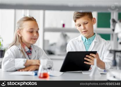education, science and technology concept - kids with tablet pc computer studying chemistry at school laboratory. kids with tablet pc at school laboratory
