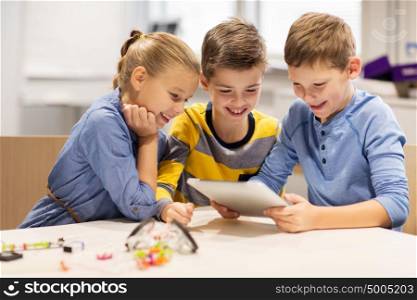 education, science, technology, children and people concept - group of happy kids or students with tablet pc computer programming electric toys and building robots at robotics school lesson. kids with tablet pc programming at robotics school