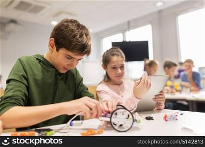 education, science, technology, children and people concept - group of happy kids or students with tablet pc computer programming electric toys and building robots at robotics school lesson. kids with tablet pc programming at robotics school