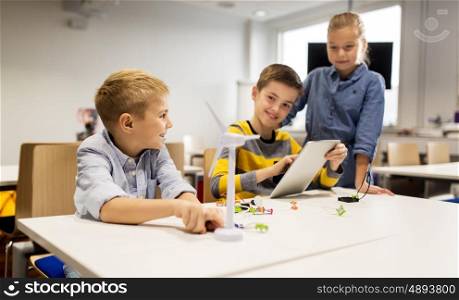 education, science, technology, children and people concept - group of smiling kids or students with tablet pc computer programming electric windmill toy at robotics school lesson