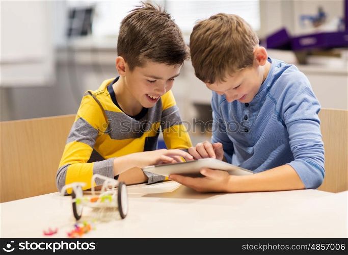 education, science, technology, children and people concept - happy boys or students with tablet pc computer programming electric toys at robotics school lesson