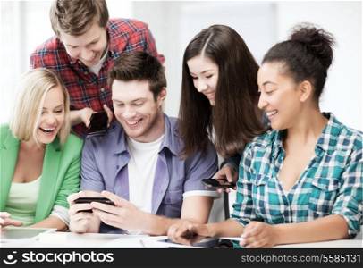 education, smatphones and internet - smiling students looking at smartphone at school