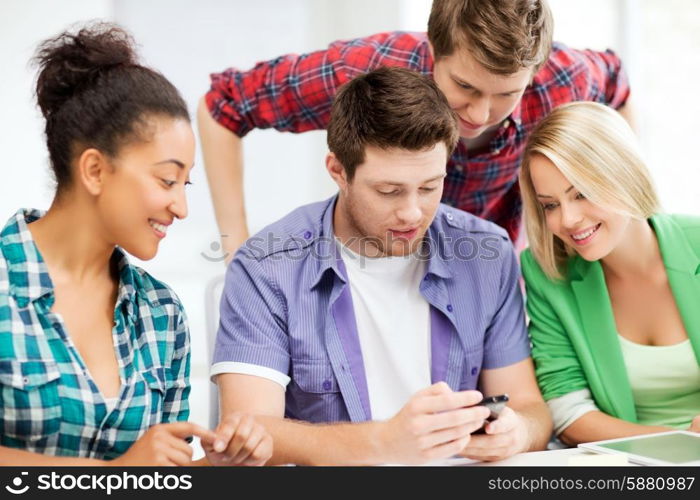 education, smatphones and internet - smiling students looking at smartphone at school